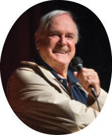 Cleese on stage with a microphone.