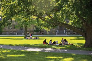 Reunioners sit in the shade of a tree on the Arts quad