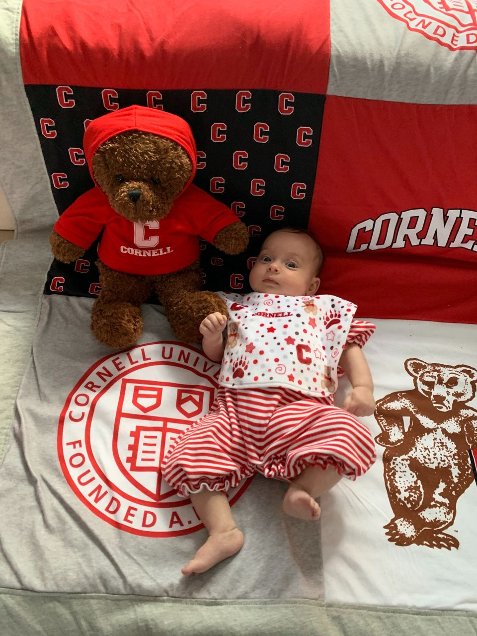 An infant lies on a Cornell blanket, surrounded by CU swag.